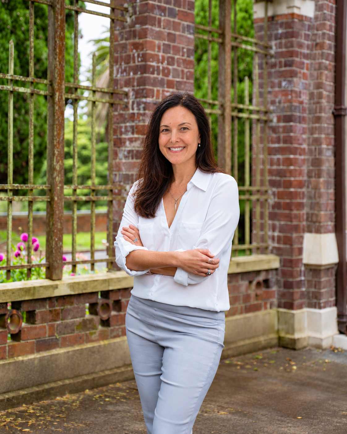Janeen Anyon smiling outdoors beside a brick and iron garden fence